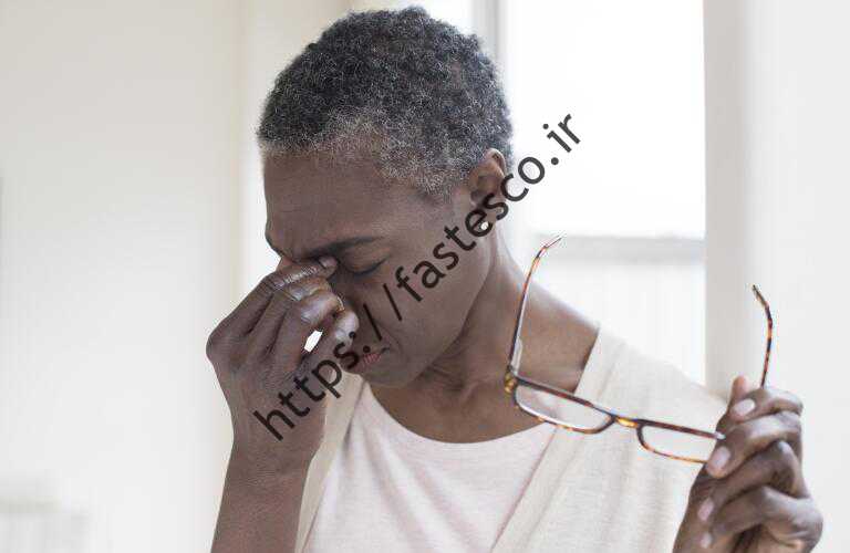 یک زن میانسال آفریقایی آمریکایی عینک را برمی دارد و بینی خود را می فشارد